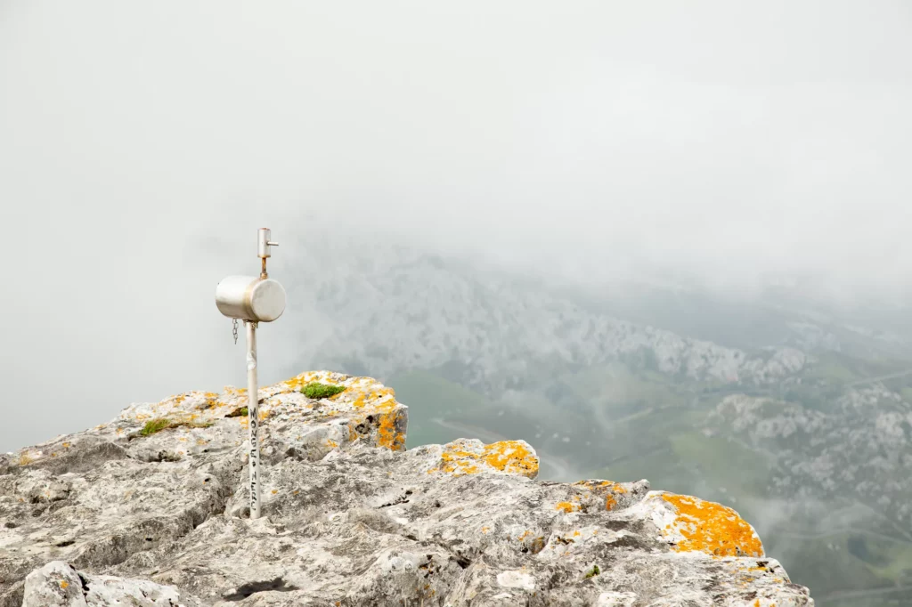 Buzón de sommet sur un rocher couvert de lichen orange, dans les nuages