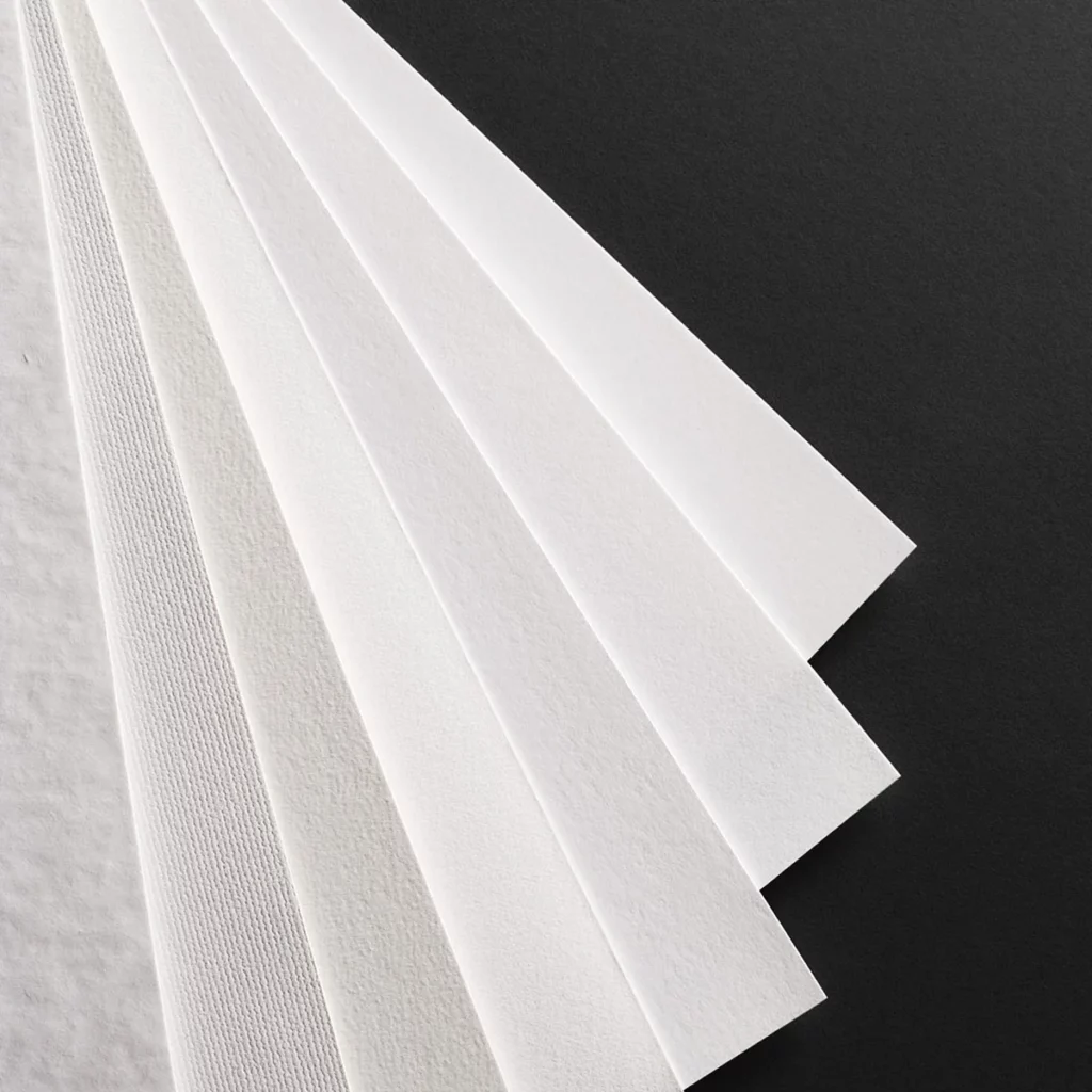 Feuilles de papier d’art blanches de textures différentes disposées en éventail sur fond noir