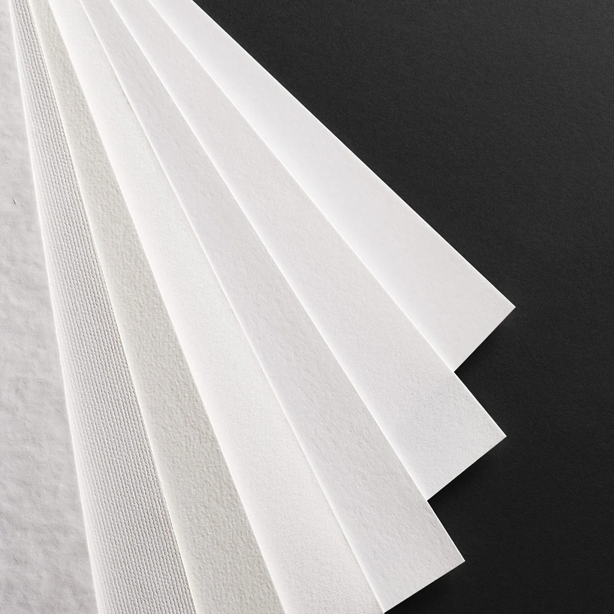 Feuilles de papier d’art blanches de textures différentes disposées en éventail sur fond noir